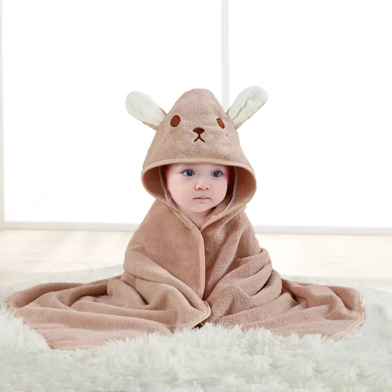 A baby wearing a brown fuzzy hooded bathrobe with cartoon animal ears lying on a white rug.