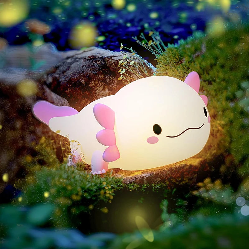 A glowing pink axolotl night light rests on mossy rocks in a dark, natural setting.