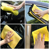 Hands cleaning a car window with yellow microfiber towels.