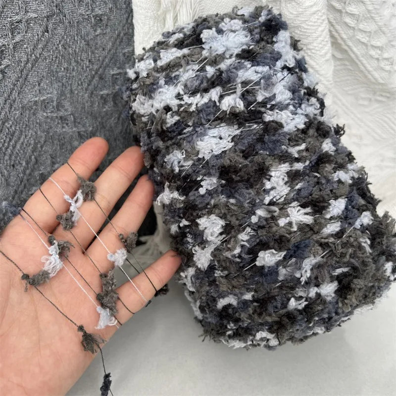 A hand is holding a skein of hand-dyed variegated grey and white yarn for knitting or crochet.
