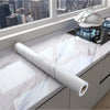 Roll of white marble peel-and-stick wallpaper displayed on a kitchen countertop with a silver serving dish in the background.
