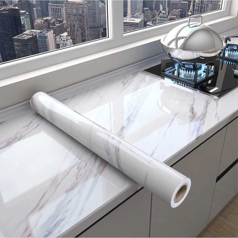 Roll of white marble peel-and-stick wallpaper displayed on a kitchen countertop with a silver serving dish in the background.