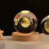 A spherical crystal ball night light with a golden sphere inside, resting on a natural wooden base.