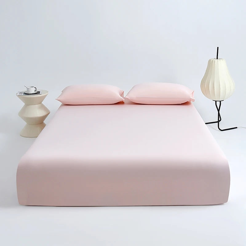 A pink cooling ice-silk fitted sheet with two pillows is displayed on a white surface next to a light fixture.
