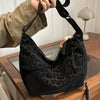 A black leopard print crossbody bag is being held by a hand, resting on a wooden surface.