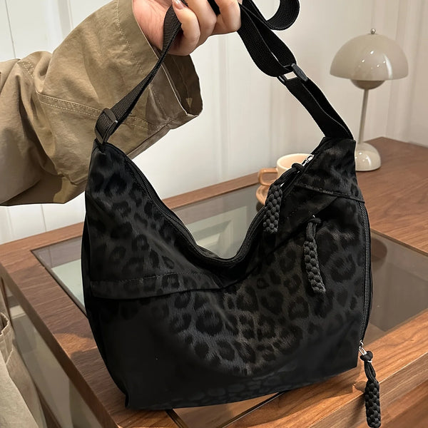 A black leopard print crossbody bag is being held by a hand, resting on a wooden surface.