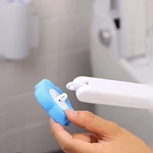 A hand is holding a white toilet brush with a blue cleaning pad and wall-mount holder.