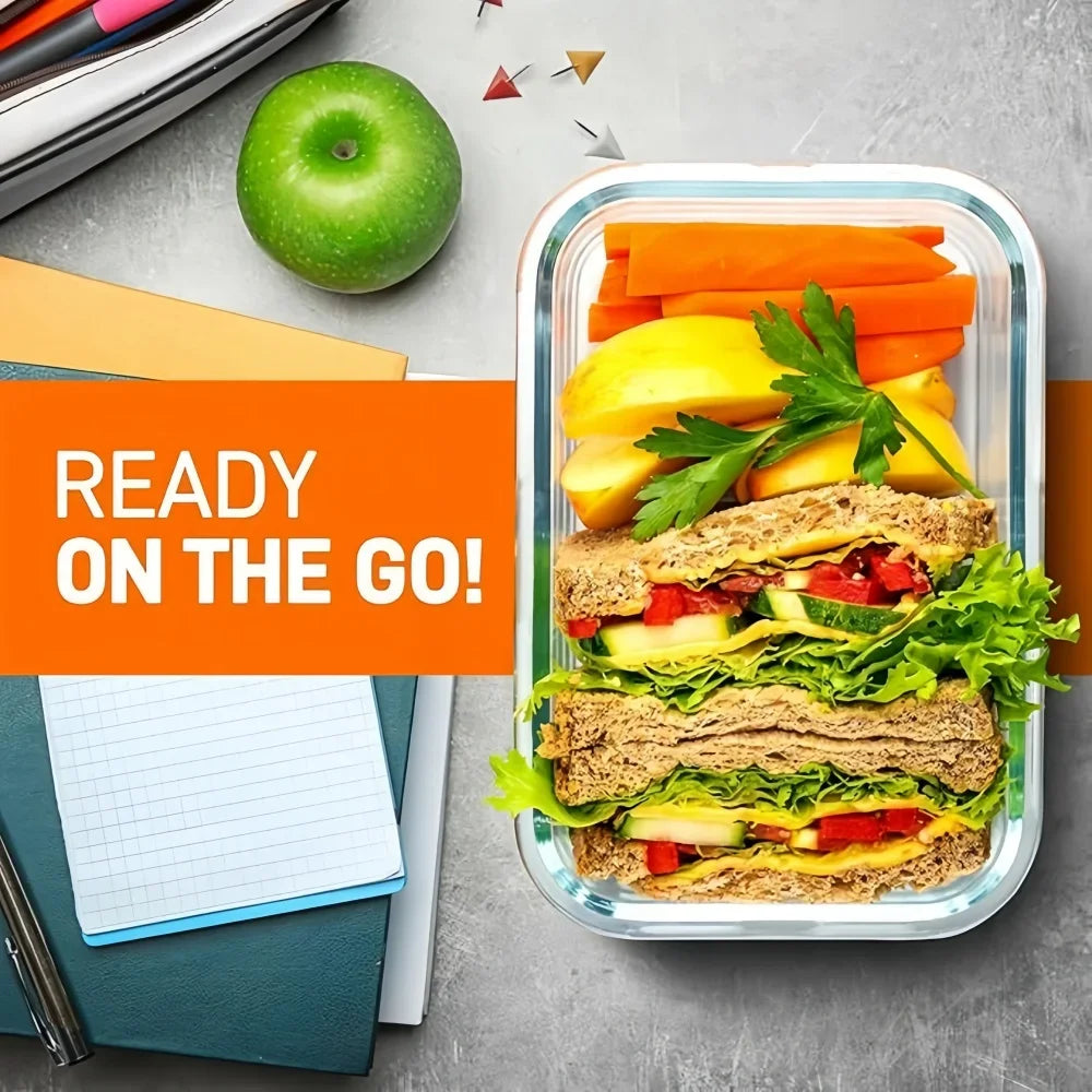 A rectangular glass lunch box filled with a sandwich, vegetables, and greens, set on a gray surface.
