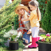 A young girl is holding a grow bag while standing outdoors with plants and gardening tools.
