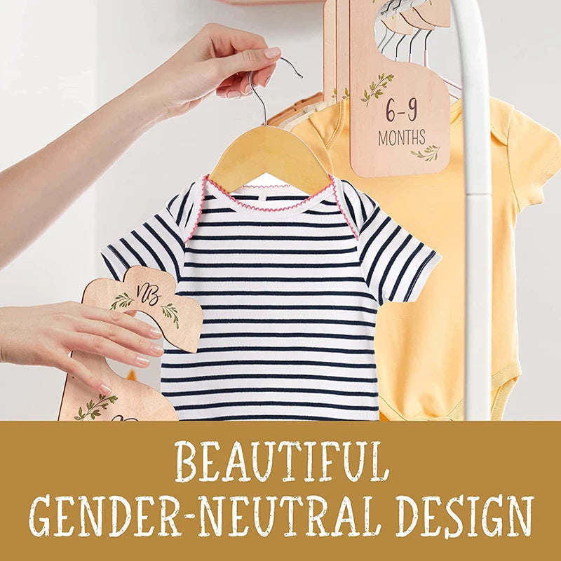 A yellow baby shirt is hanging on a wooden hanger next to pink and natural wood closet dividers.