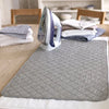 A gray quilted ironing mat is placed on a wooden table next to a handheld garment steamer.
