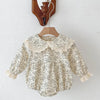 A cream floral lace cotton romper for a baby girl hanging on a wooden hanger.