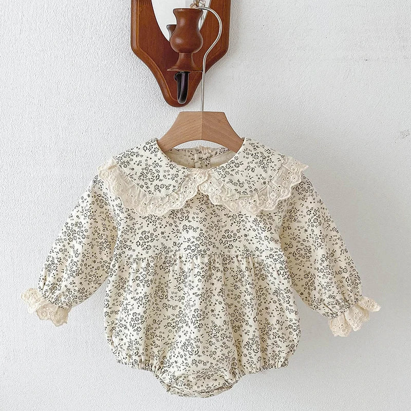 A cream floral lace cotton romper for a baby girl hanging on a wooden hanger.