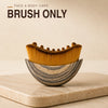 A wooden facial brush with golden bristles rests on a light stone surface.