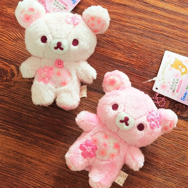 A pink cherry blossom plush bear keychain is shown resting on a wooden surface.