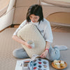 A person is reading a book while resting their head on a beige foam inflatable camping pillow in an outdoor tent setting.