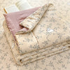 A stack of light beige quilt fabric featuring a delicate blue floral pattern and small white rabbit illustrations.