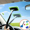 A hand is operating a car windshield cleaning brush kit with a green microfiber pad inside a vehicle.