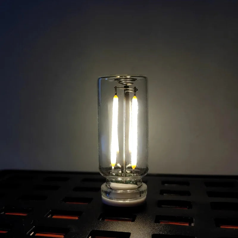 A clear glass LED night light with a warm filament glow is displayed on a dark surface.