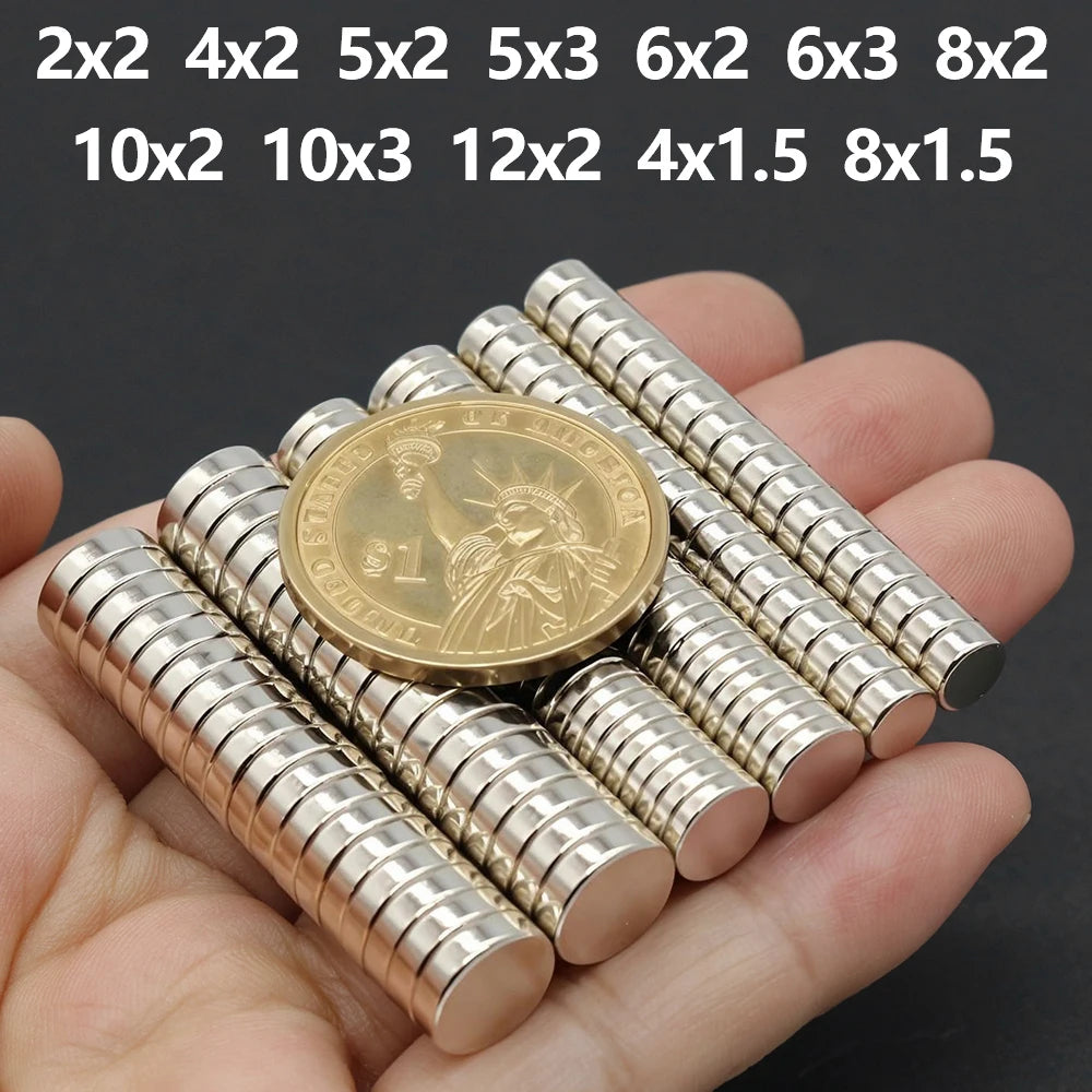 A hand holds several small silver disc magnets with various sizes and shapes.