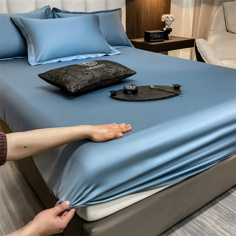 Un juego de sábanas ajustadas de algodón de lujo azul claro está tendido sobre una cama, con una mano ajustando la tela.