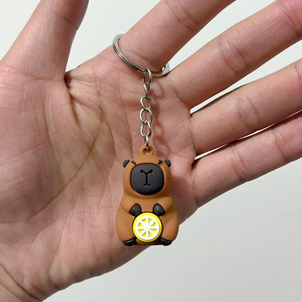 A small brown capybara charm with a yellow citrus slice detail is being held on a person's finger.