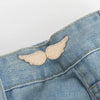 A small, light gold glitter angel-shaped brooch pinned onto a blue denim jean fabric.