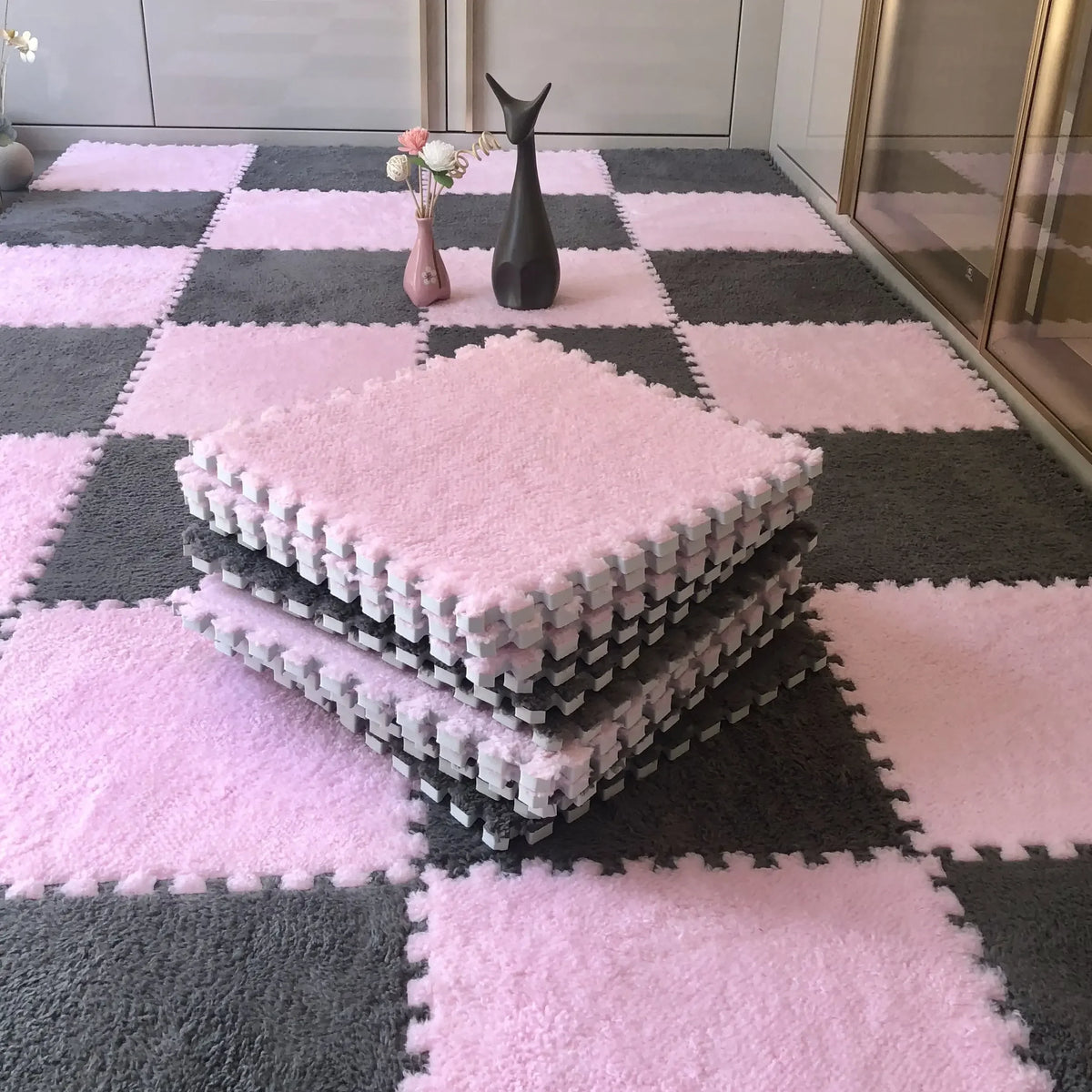 Pink and gray interlocking floor tiles with a stack of pink plush mats on the surface.