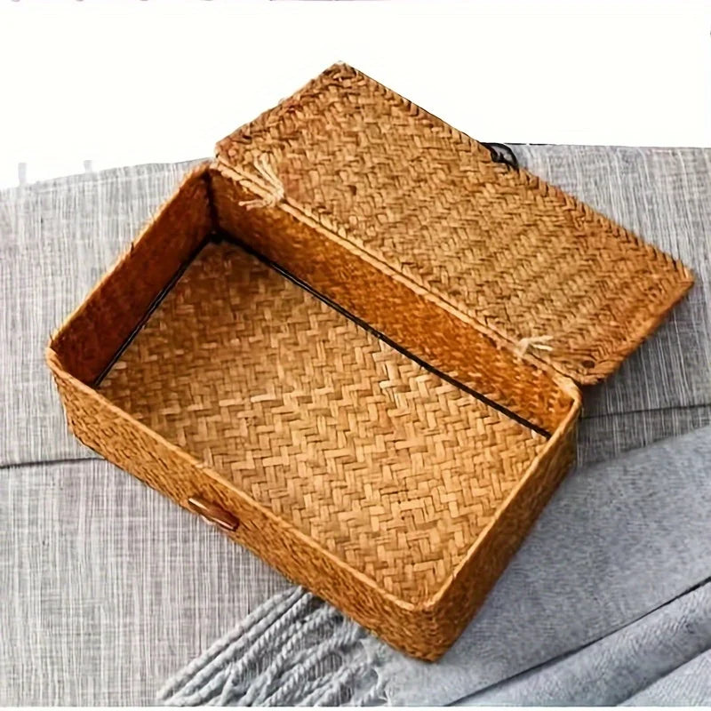 A square woven rattan storage basket with a lid resting on a gray fabric surface.