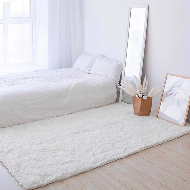 Extra large white Nordic fur rug placed on a light wood floor next to a bed and mirror.