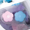 Pink and blue flower shaped lint and hair catcher filter bags floating in soapy water inside a washing machine drum