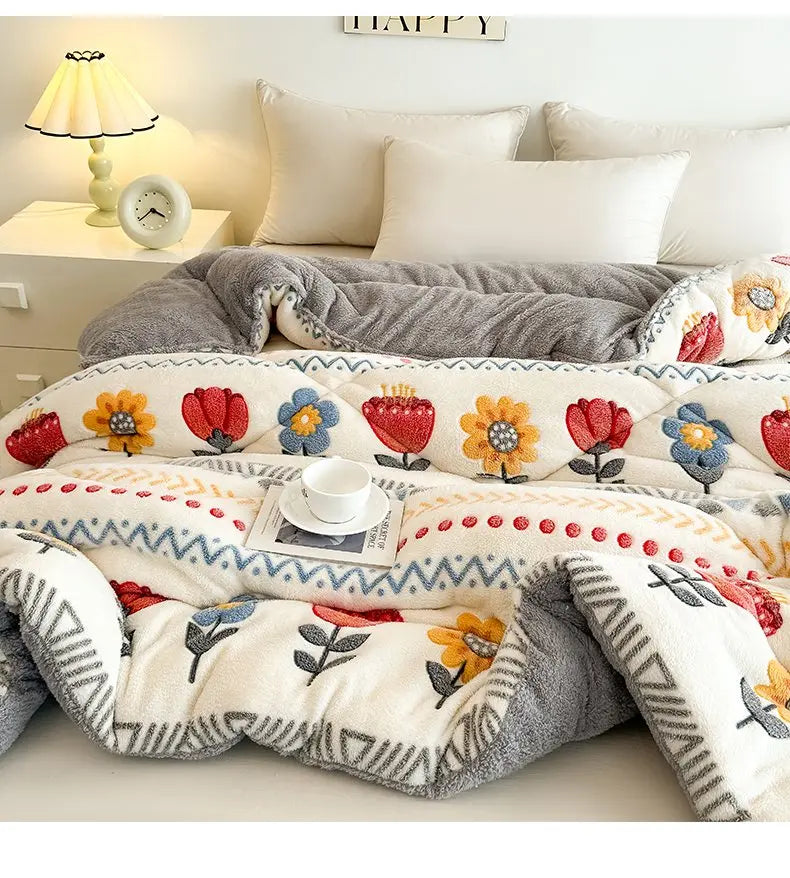 A cozy, multi-patterned plush throw blanket featuring floral designs in orange, red, and blue on a white background.