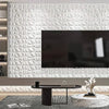 A modern living room featuring a large television mounted on a white, textured diamond wall panel and wooden furniture.