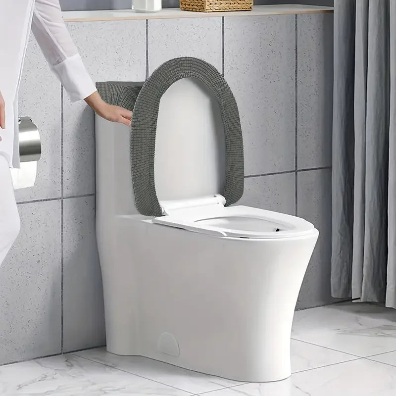 A white toilet with a gray fleece seat cover and lid, being adjusted by a person.