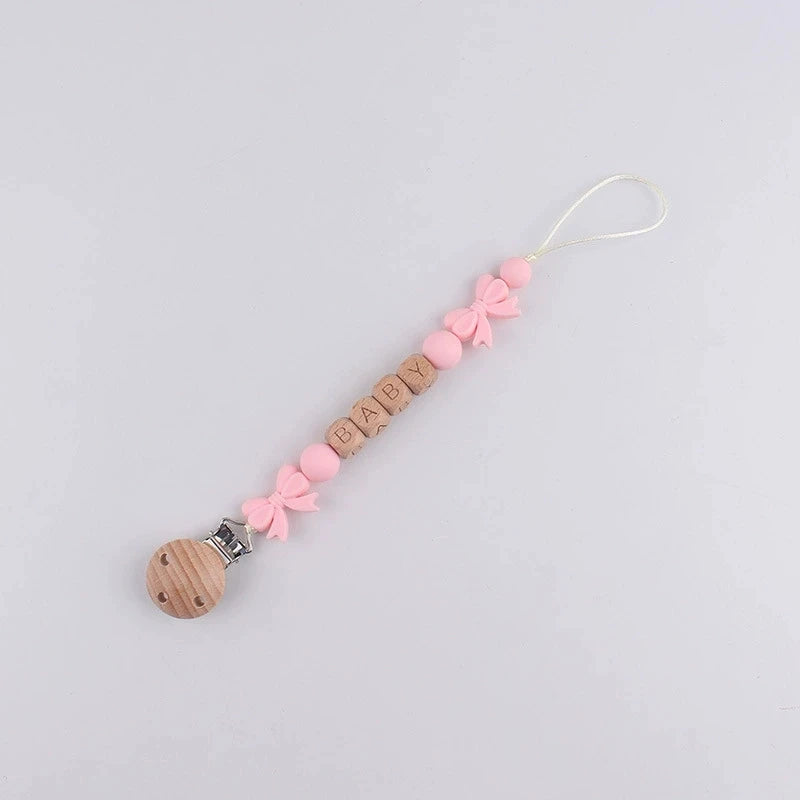 A pink silicone pacifier clip with a wooden attachment and a floral ribbon lanyard.