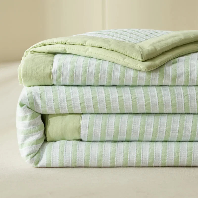 A stack of light green and white striped breathable summer quilts.