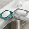 A self-draining silicone soap tray with elevated ridges is placed in a kitchen sink, featuring a white bar of soap.