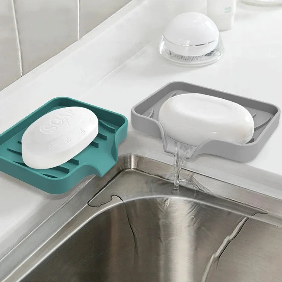 A self-draining silicone soap tray with elevated ridges is placed in a kitchen sink, featuring a white bar of soap.