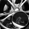 Close-up view of four knurled aluminum tire valve caps mounted on a silver alloy wheel rim.