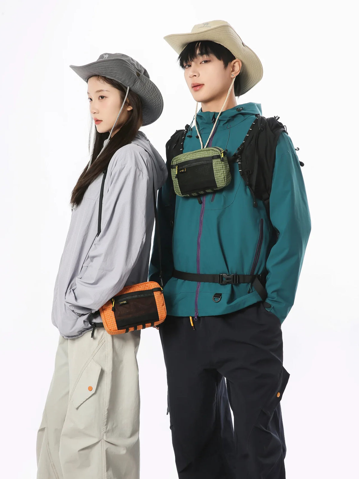 A young man and woman standing side by side, wearing outdoor-inspired clothing and a tactical waist bag.