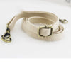 A beige canvas shoulder strap with a brass buckle is shown lying on a white background.