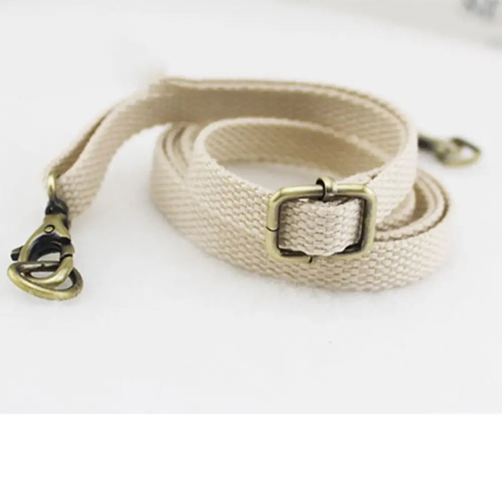 A beige canvas shoulder strap with a brass buckle is shown lying on a white background.