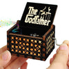 A hand holding a vintage hand-crank wooden music box with an open lid displaying the name Godfamer.
