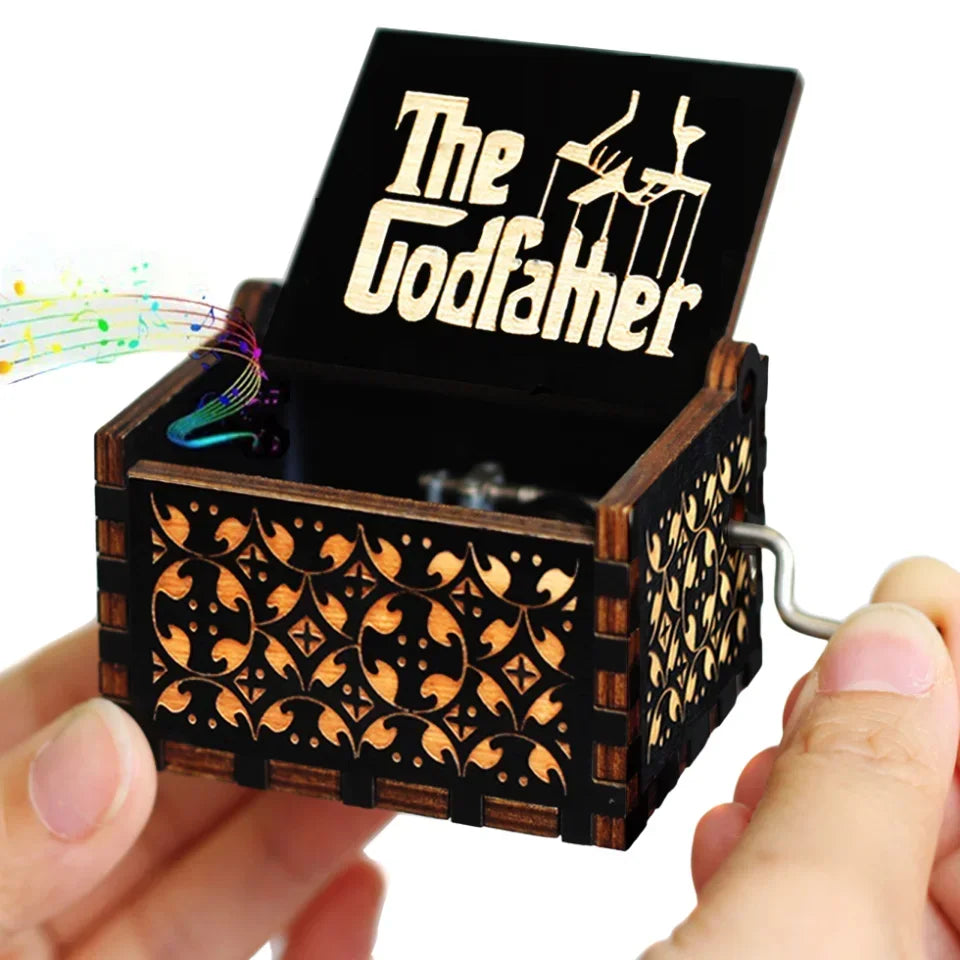 A hand holding a vintage hand-crank wooden music box with an open lid displaying the name Godfamer.