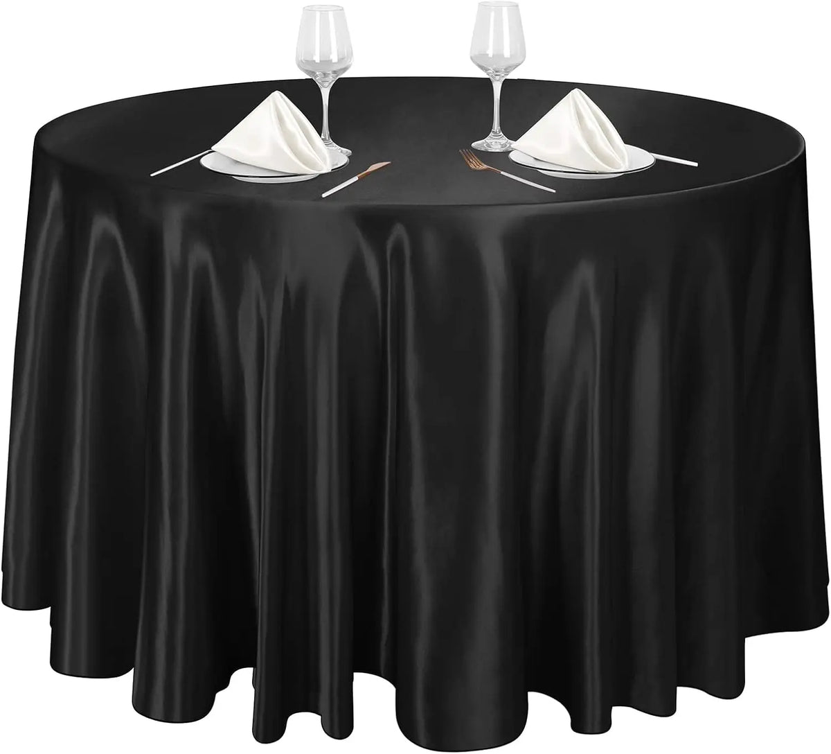 A black satin tablecloth set for a round table with wine glasses and napkins.