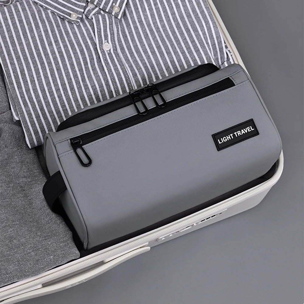 A gray toiletry bag with a black carry handle is shown inside a light-colored case, next to a striped shirt.