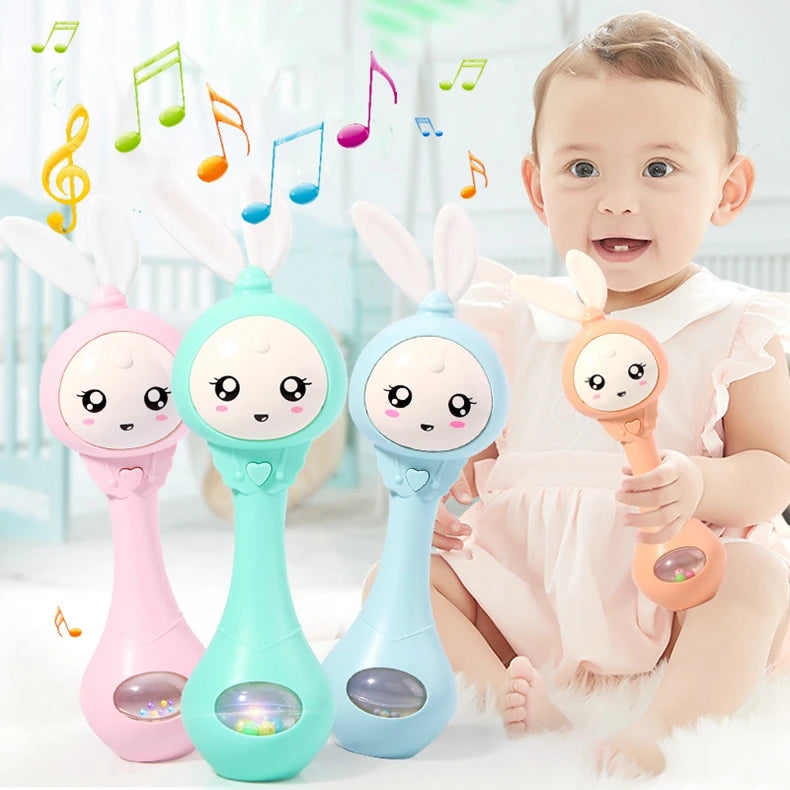 A baby is holding a pink and teal musical rabbit rattle teether toy.