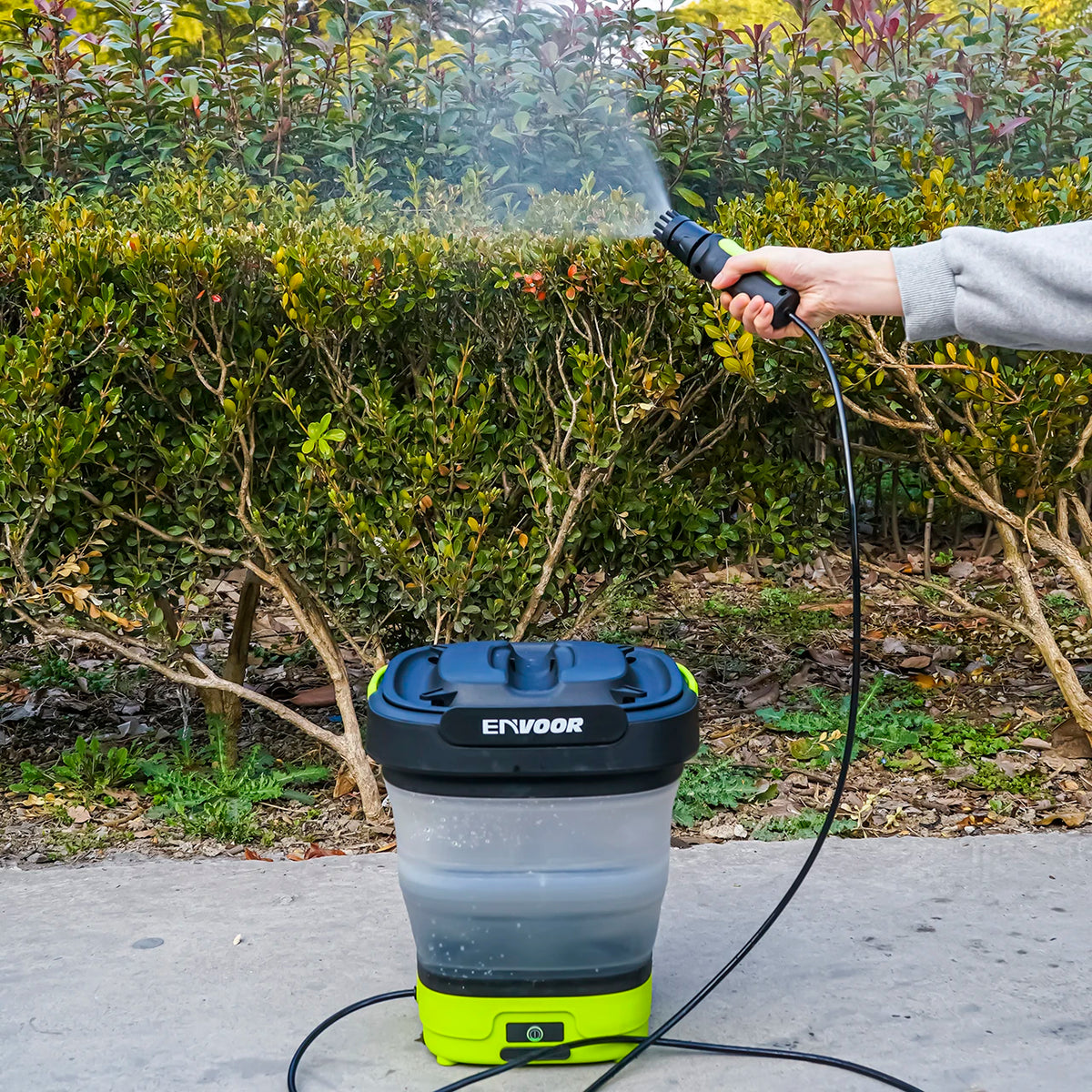 Eine Hand sprüht Wasser mit einer portablen Elektrodruckwaschmaschine auf einen grünen Busch.