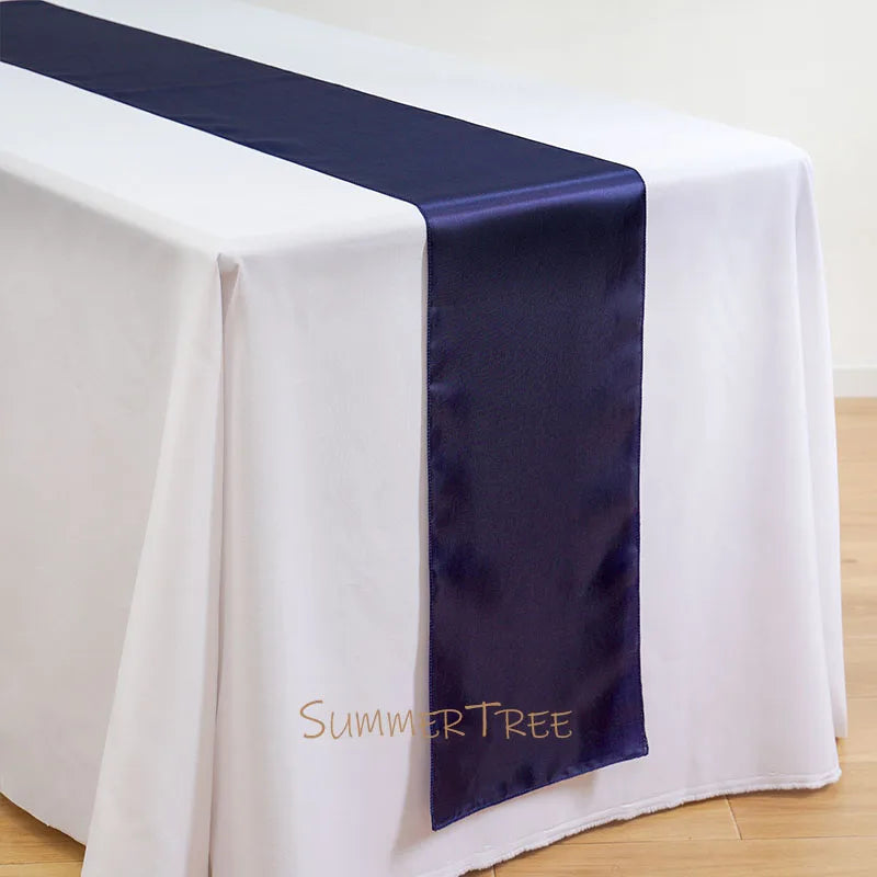 Elegant satin table runner in navy blue laid across a white tablecloth.