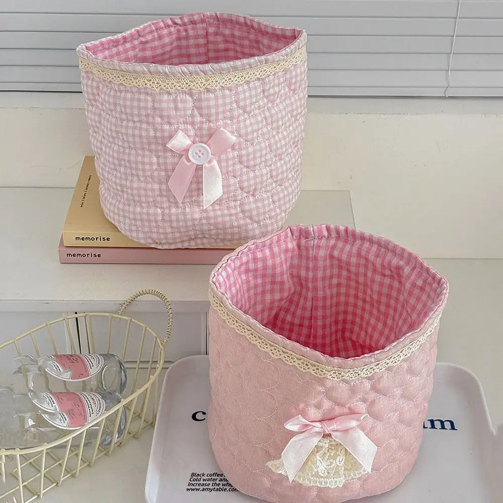 Cesta de guardado para colchas rosa con detalle de corazón y ribete amarillo sobre una bandeja blanca.